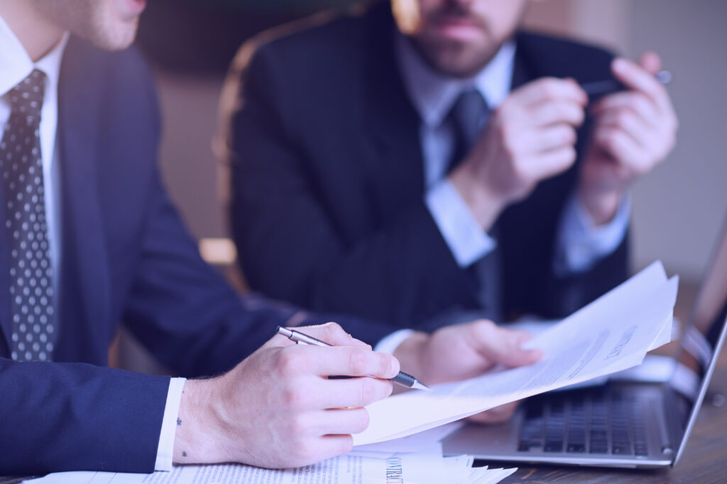 Certidão Negativa de Débitos Trabalhistas: dois homens conversam, um segurando folhas de papel e uma caneta, enquanto à sua frente há um notebook.