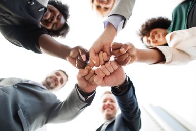 5 pessoas juntando as mãos no centro da imagem usada para representar profissionais responsáveis por treinamentos de segurança do trabalho