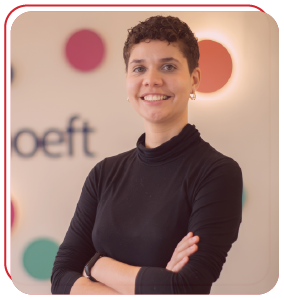 Funcionária Bernhoeft sorrindo para a câmera com os braços cruzados abaixo dos seios. Ela é uma mulher branca, cabelos curtos e veste camisa preta.