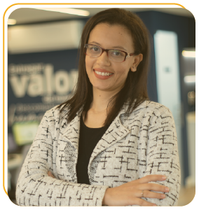 Funcionária Bernhoeft sorrindo para a câmera. Ela é uma mulher branca, com cabelos pretos, lisos até os ombros. Veste camisa preta e blazer branco com estampas retangulares na cor preta.