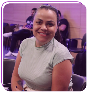 Mulher sentada e sorrindo olhando para a câmera vestindo uma blusa de cor verde água