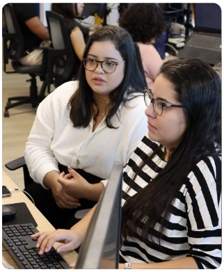 duas funcionárias sentadas olhando para um monitor à sua frente.