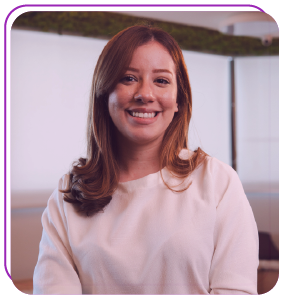Funcionária bernhoeft sorri para a foto. Ela é ruiva, cabelo tamanho médio, tem a pele branca e veste uma camisa de manga longa na cor branca.