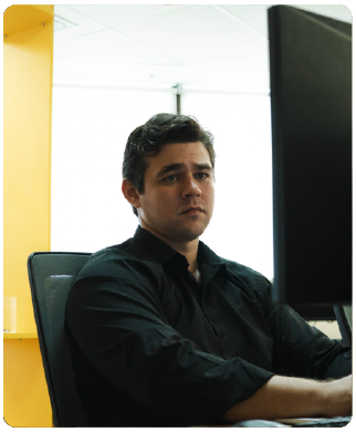 Funcionário Bernhoeft sentado olhando para o computador. Ele é branco, veste uma camisa de manga longa na cor preta.