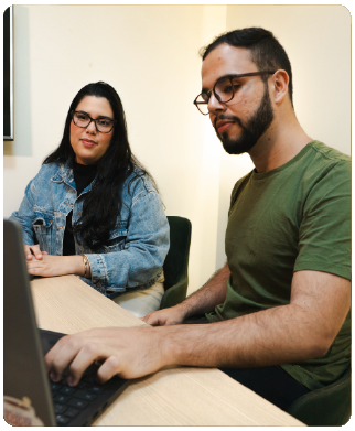Dois funcionários bernhoeft, um homem e uma mulher. Ambos sentados olhando para um computador em comum.